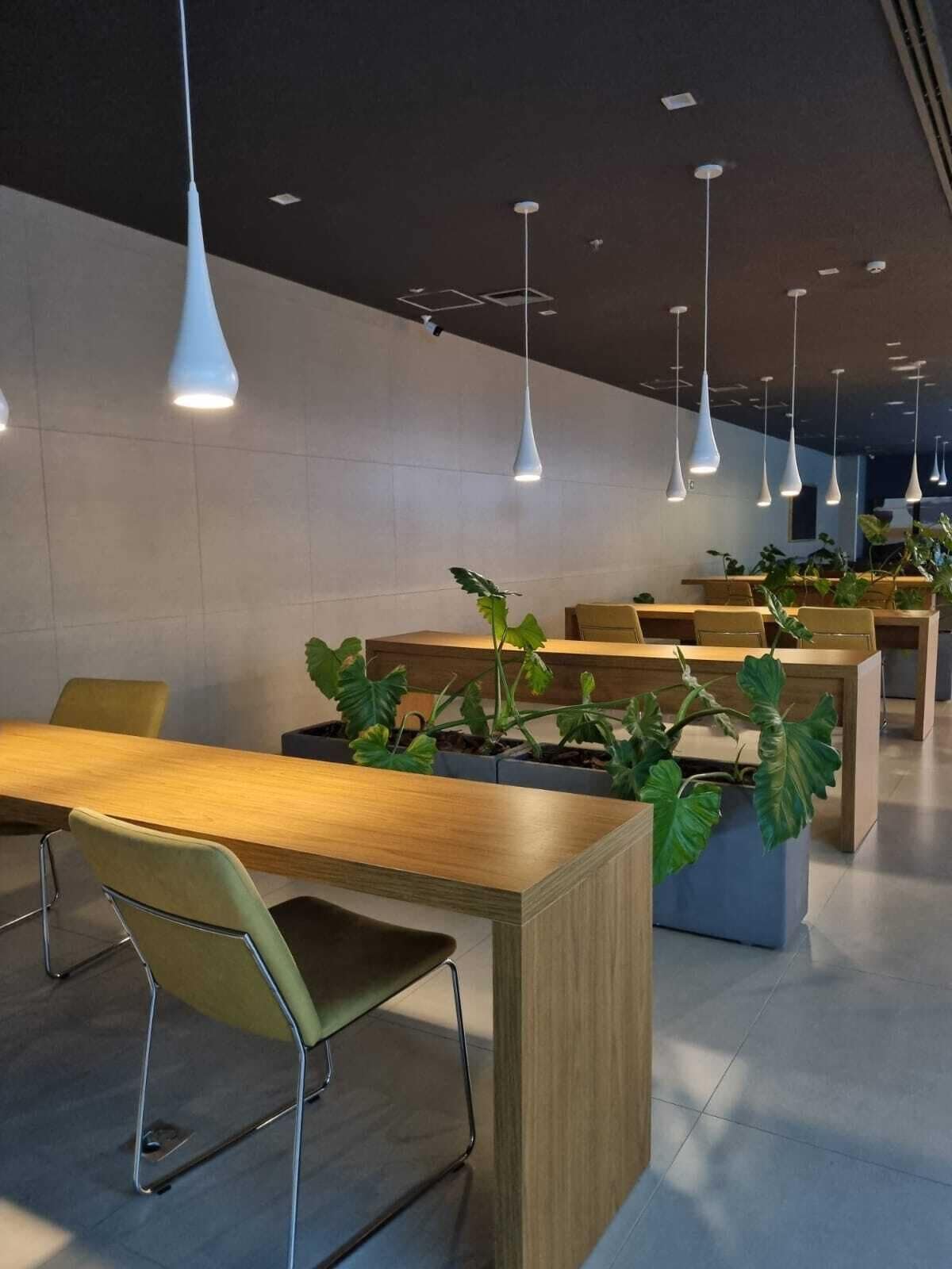 A modern indoor space with multiple tables and chairs, pendant lighting, and potted plants.