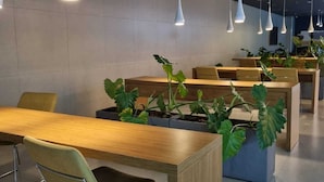 A modern indoor space with multiple tables and chairs, pendant lighting, and potted plants. - Studio Premium Augusta | Next Oscar Freire (São Paulo)