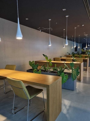 A modern indoor space with multiple tables and chairs, pendant lighting, and potted plants. - Studio Premium Augusta | Next Oscar Freire (São Paulo)