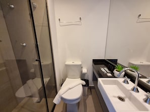 A modern bathroom with a glass shower enclosure, a toilet, a sink with a mirror, and a small potted plant. - Studio Premium Augusta | Next Oscar Freire (São Paulo)