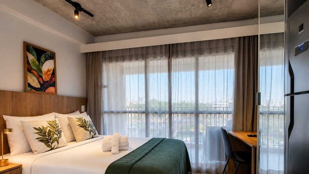 A hotel room with a bed, a desk, and a view of the city. - Studio Premium Augusta | Next Oscar Freire (São Paulo)
