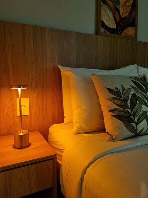 A neatly made bed with white linens and a single decorative pillow with a leaf pattern. - Studio Premium Augusta | Next Oscar Freire (São Paulo)
