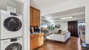 A laundry area with a washing machine and dryer, a kitchen with wooden cabinets, a dining area with a table and chairs, and a living room with a sofa and a coffee table.