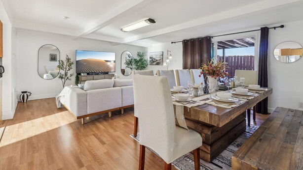 A modern living room with a sofa, dining table set for four, and a large TV.