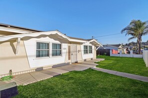 A single-story mobile home with a front porch, a small attached garage, and a well-maintained lawn. - Gated Yard, King Bed, 2 Living Rooms, Ranch Style (Spring Valley)
