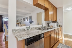 A modern kitchen with granite countertops, stainless steel appliances, wooden cabinets, and a dishwasher.