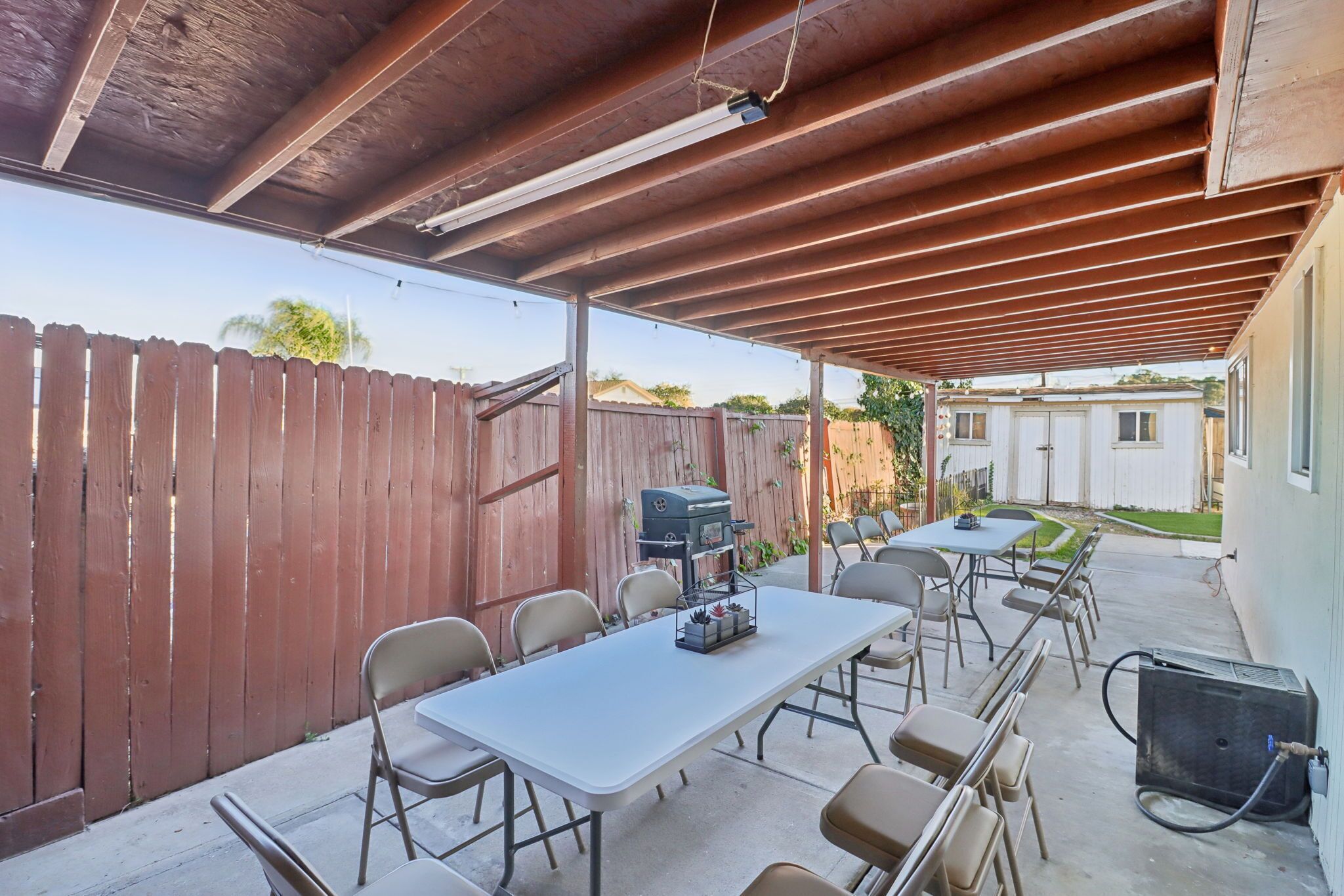 Un patio exterior con zona cubierta, una mesa, sillas, una parrilla y un calentador portátil.