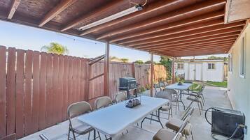 Un patio exterior con zona cubierta, una mesa, sillas, una parrilla y un calentador portátil.