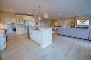 A modern kitchen with white cabinetry, a central island, and pendant lighting. - The Salty St. Louis (Ocean City)
