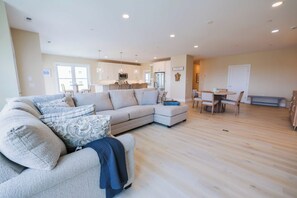 A spacious living area with a large L-shaped sofa, a dining table with chairs, and a kitchen in the background. - The Salty St. Louis (Ocean City)