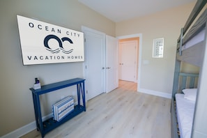 A room with a bunk bed, a console table with a sign, and a door leading to another room. - The Salty St. Louis (Ocean City)