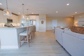 A modern kitchen with a central island, bar stools, a dining area with a sofa, and a wooden cabinet. - The Salty St. Louis (Ocean City)
