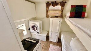 Une pièce de taille modeste comprenant un lave-linge, un petit meuble de rangement, un lit et une fenêtre avec des rideaux.