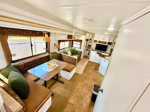 A compact RV interior with a kitchenette, seating area, and a television.