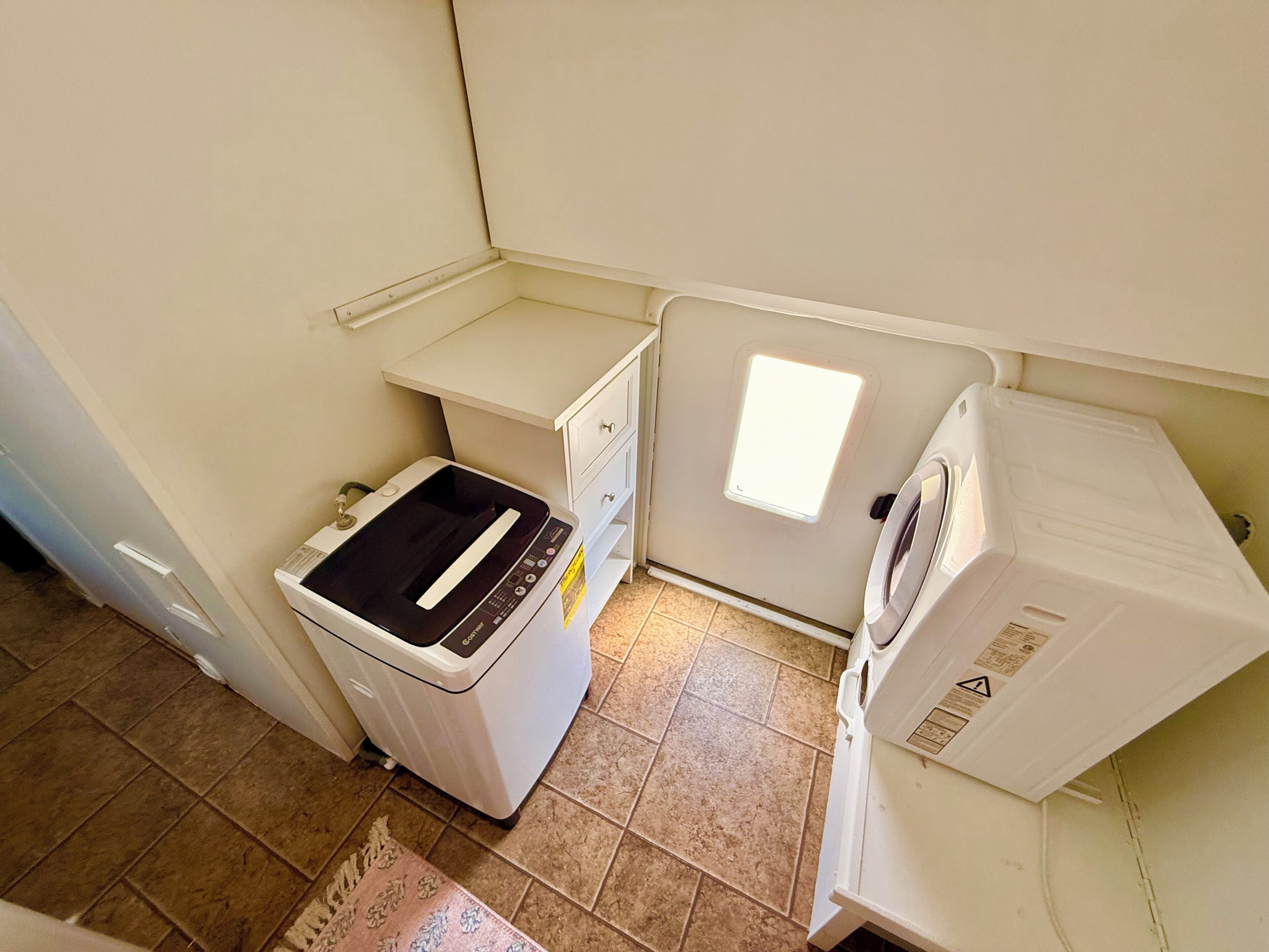 Een kleine wasruimte met een wasmachine, droger en een klein wasbakje.