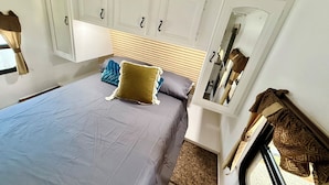 A bedroom with a bed, a headboard, a wardrobe, a mirror, and a window with curtains.