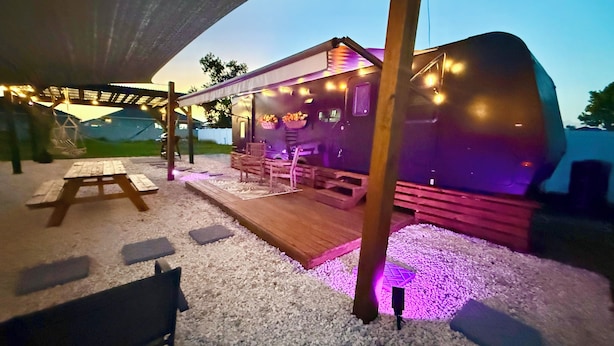 A covered outdoor seating area with tables and chairs, a wooden deck, and string lights.