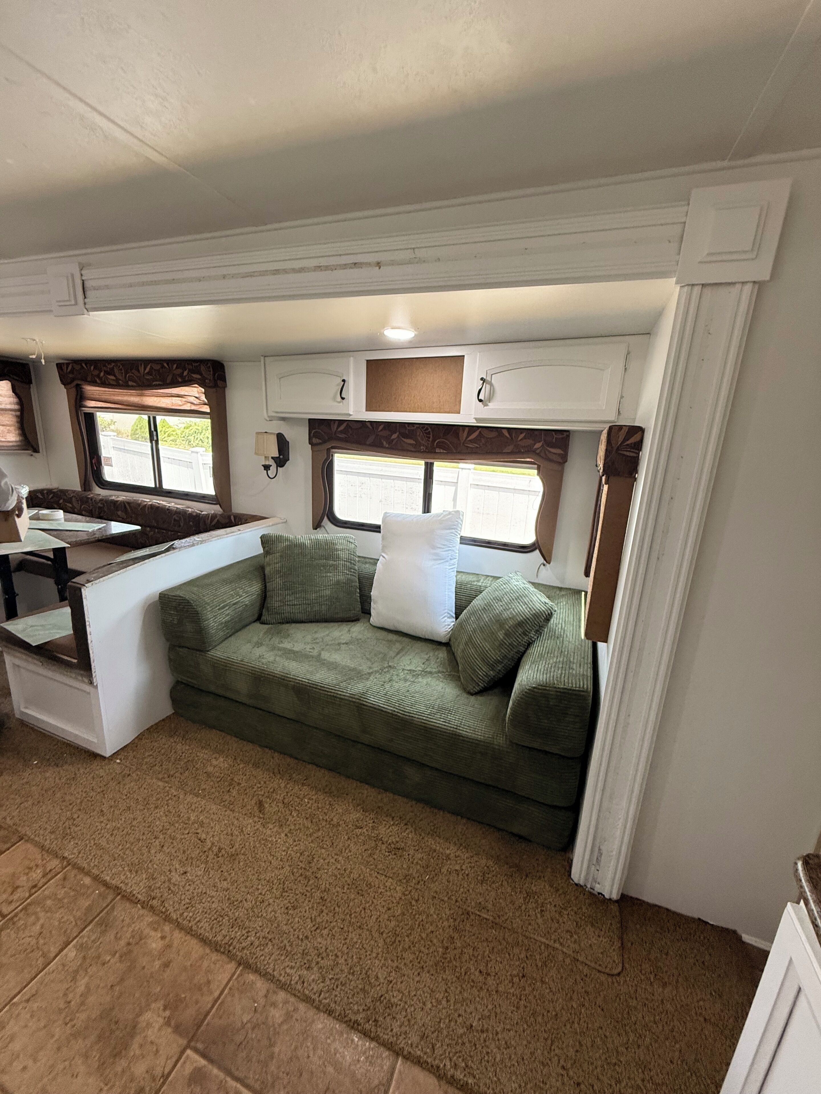Een compact RV-interieur met een kitchenette, een groene bank met kussens, en een raam dat natuurlijk licht binnenlaat.