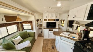 Une cuisine compacte pour camping-car, équipée d’une cuisinière intégrée, d’un évier et d’un téléviseur.