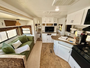 A compact RV kitchen with a built-in stove, a sink, and a television.