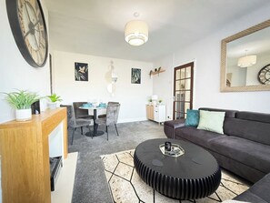 A modern living room with a sofa, a round coffee table, and a dining area with chairs and a table. - Cosy Southport Bungalow | 2 Bedroom with Parking (Banks)