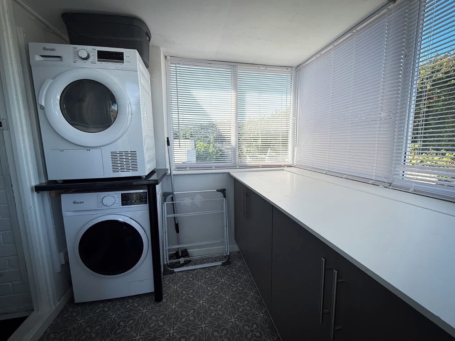 A laundry room with two washing machines, a drying rack, and a window with blinds.