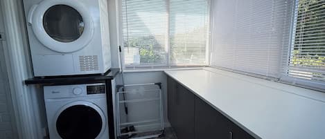 A laundry room with two washing machines, a drying rack, and a window with blinds.