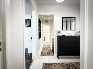 A hallway with a black cabinet, a door leading to another room, and a patterned rug. - Cosy Southport Bungalow | 2 Bedroom with Parking (Banks)