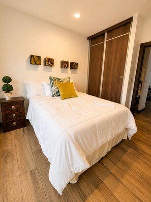 A bedroom with a large bed, wooden floor, a nightstand, a dresser, and a wardrobe. - Beautiful 2-Bedroom Apartment with Balcony in Guatemala City (Ciudad de Guatemala)