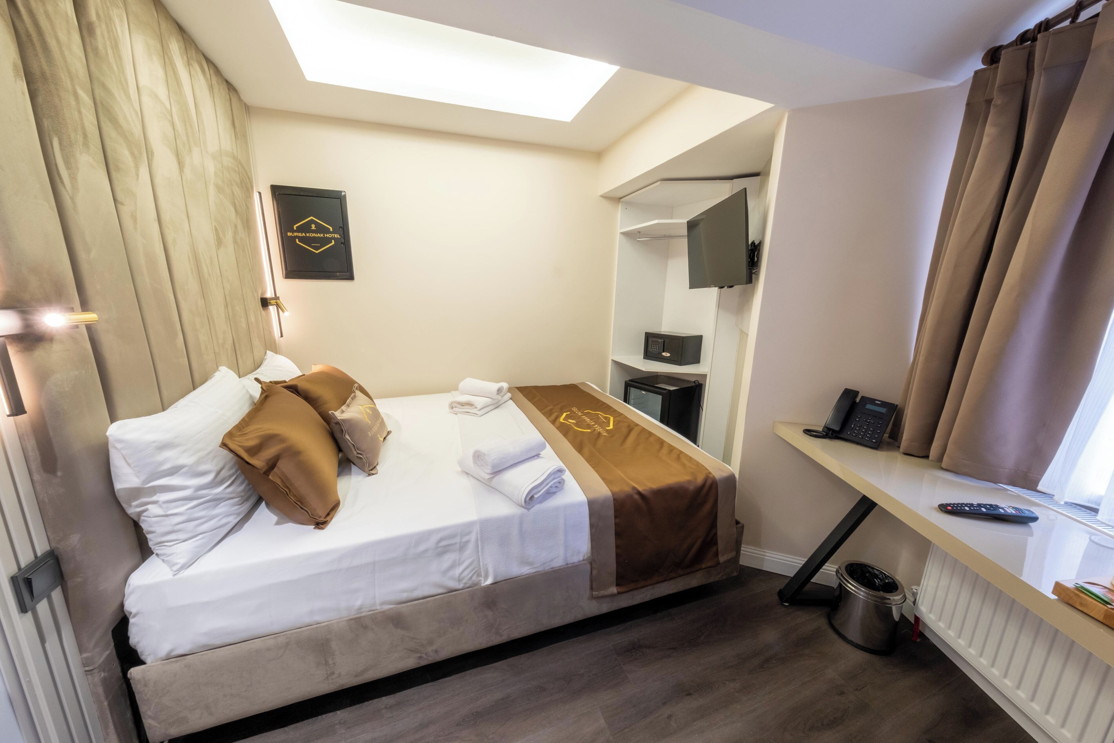 A hotel room with a bed, a desk, a mirror, a TV, and a window with curtains.