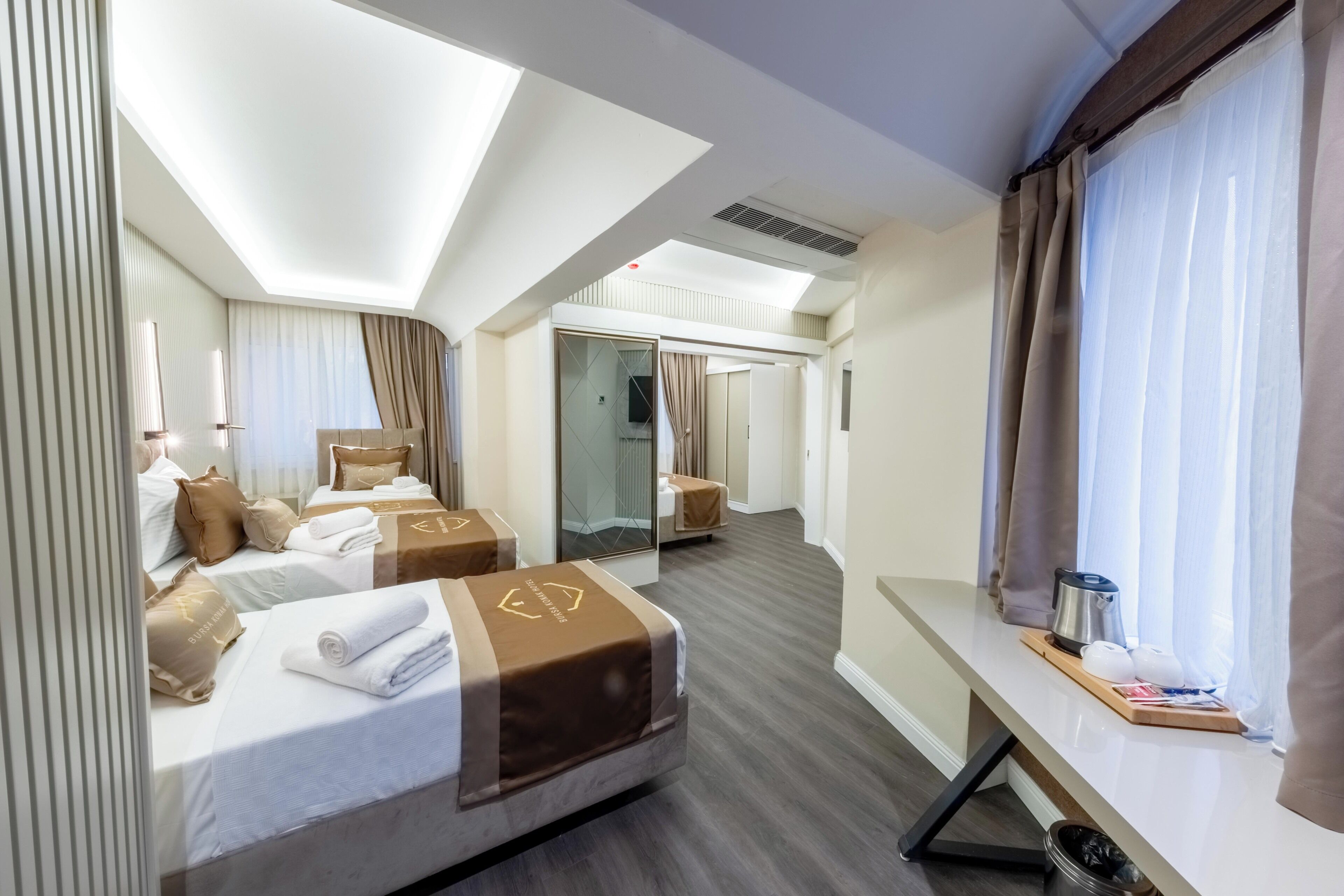 Habitación de hotel con dos camas, un escritorio, una ventana con cortinas y un espejo.