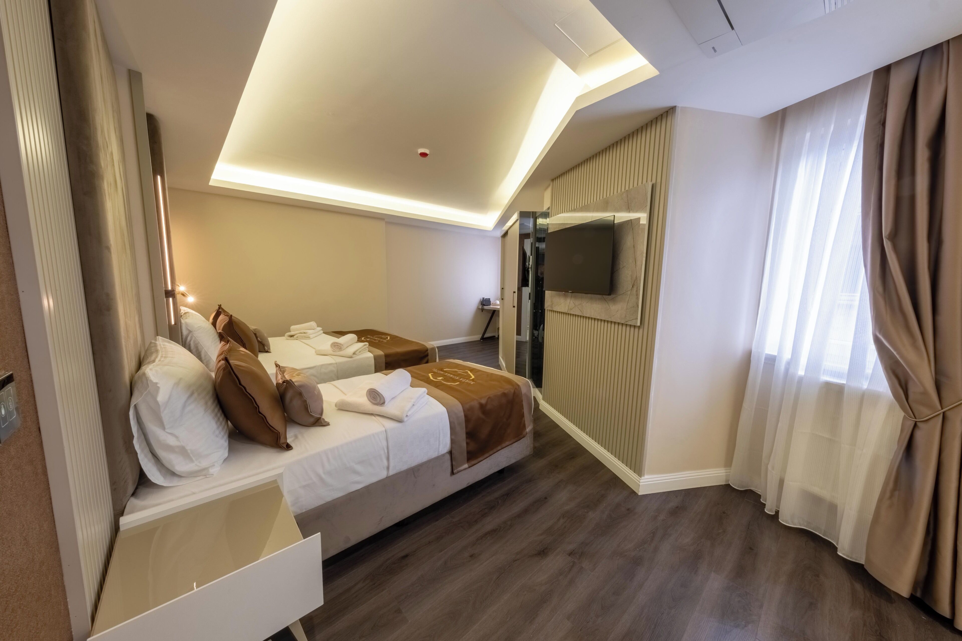 A hotel room with two beds, a TV, and a large window with curtains.