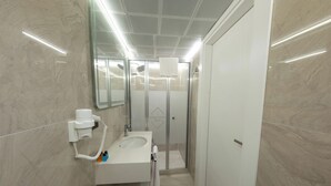 A modern bathroom with a glass shower enclosure, a built-in sink, and a hairdryer. - Bursa Konak Hotel (Bursa)