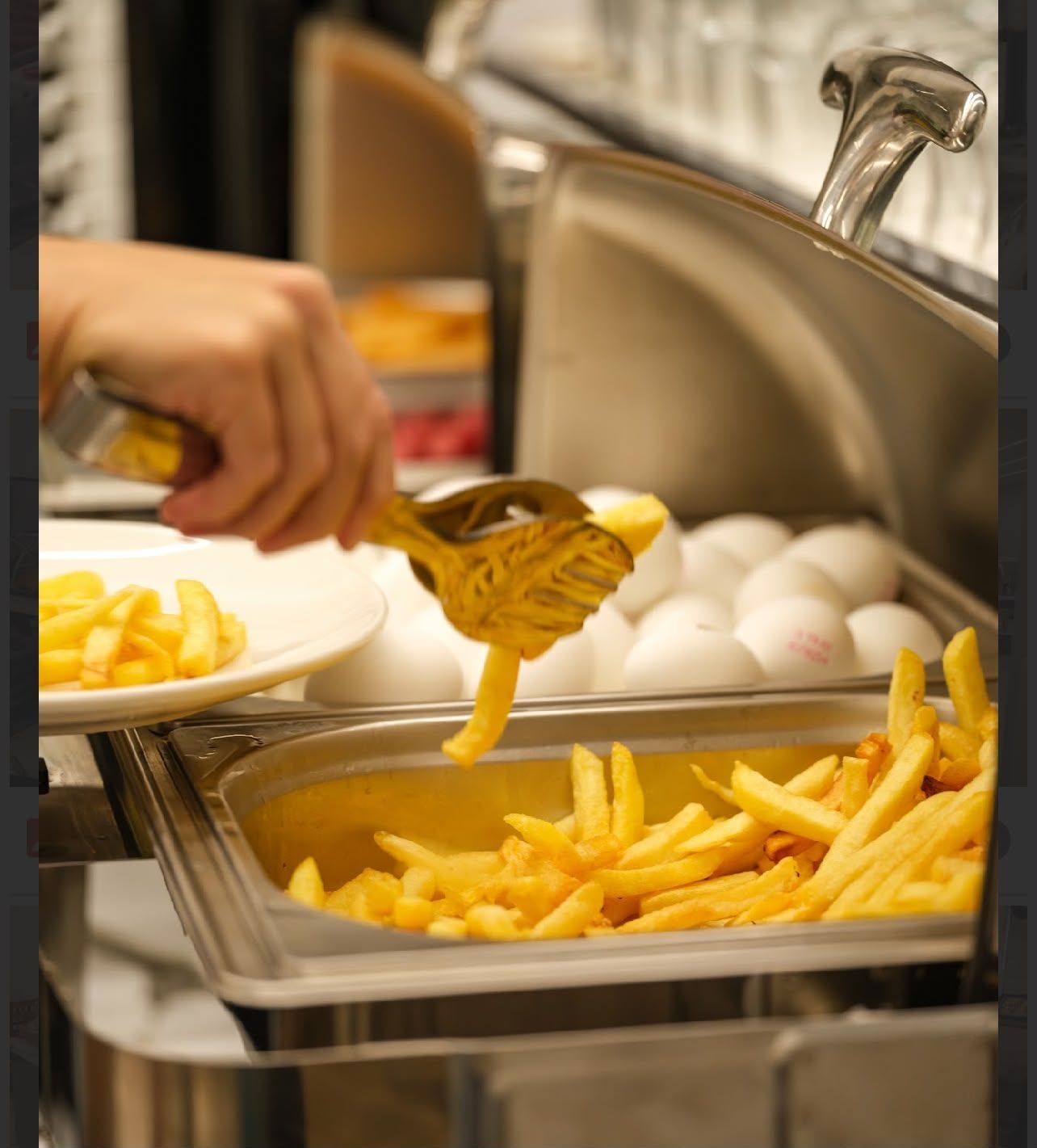 A buffet setup with a hand using a yellow slotted spoon to serve french fries.