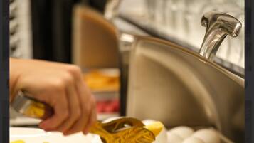 A buffet setup with a hand using a yellow slotted spoon to serve french fries.