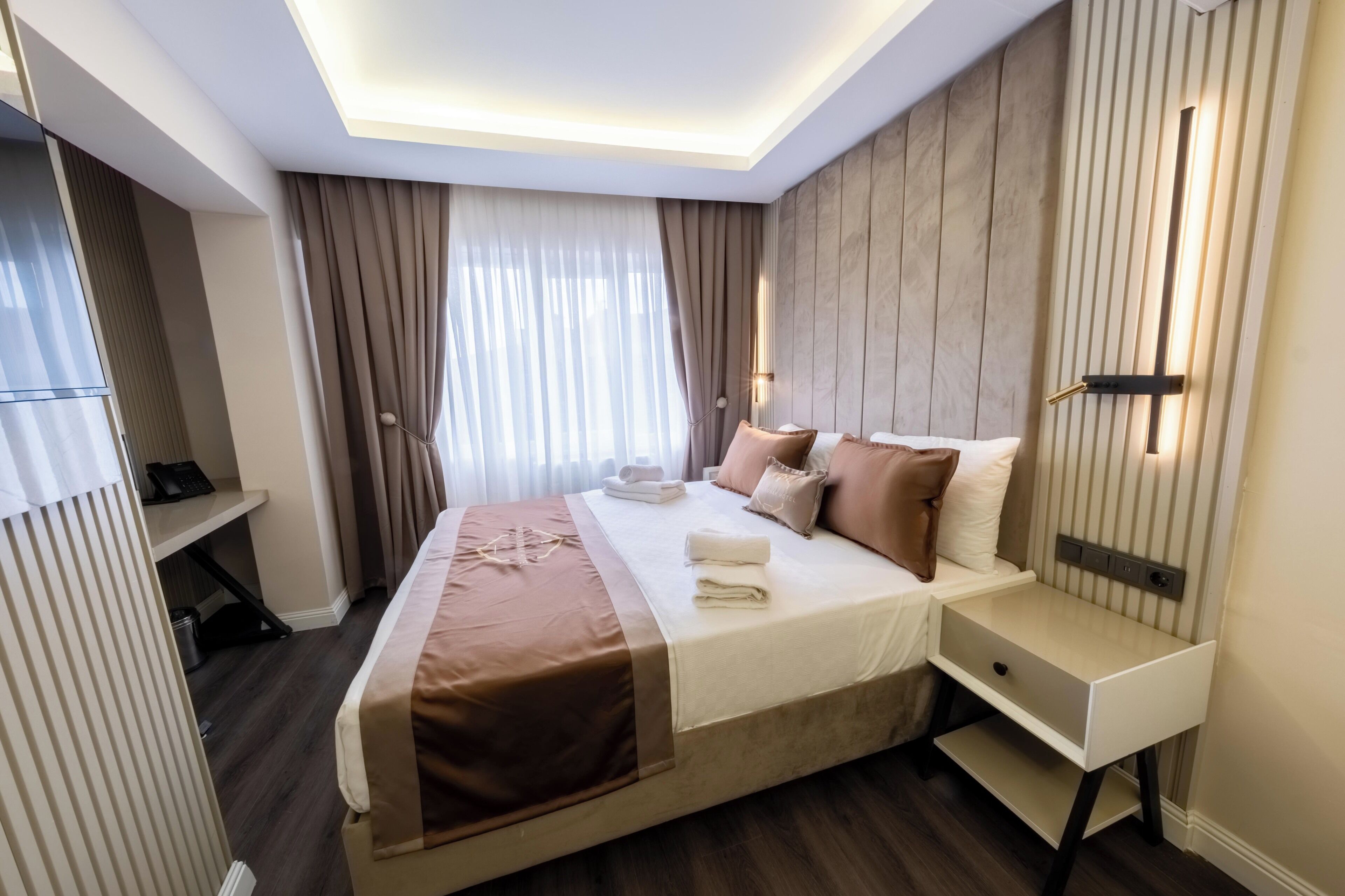 A hotel room with a bed, bedside tables, a desk, and a window with curtains.