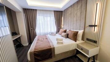 A hotel room with a bed, bedside tables, a desk, and a window with curtains.