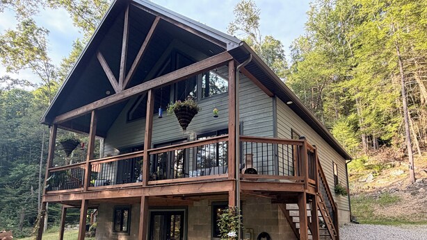 Une cabane en bois à deux étages, dotée d’un balcon, d’un espace extérieur aménagé pour s’asseoir et de fondations en pierre.