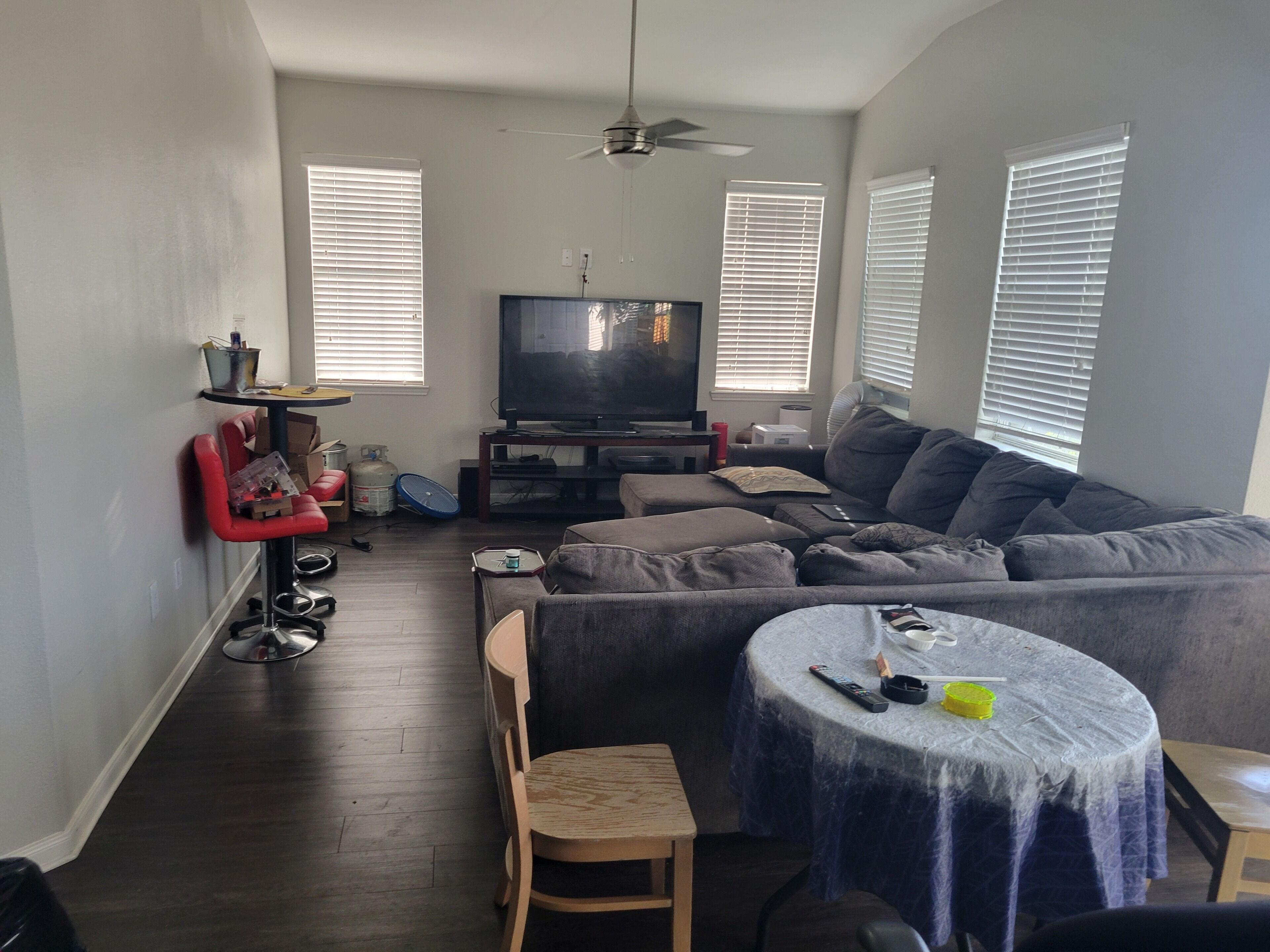 Ein Wohnzimmer mit einem grauen Sofa, einem runden Tisch, einem Fernseher und einem Deckenventilator.