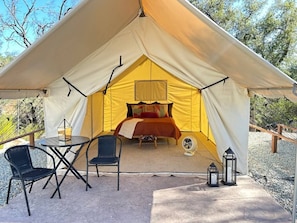 A tent with a bed, a table, two chairs, and a fan.