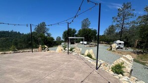 An outdoor patio area with a stone floor, a pergola with string lights, and a white RV in the background. - Moonshadow Flat Glamping Campground (Penn Valley)