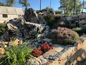 A rocky garden with a stone wall, red flowers, and a tent-like structure.