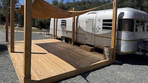 Un véhicule récréatif (VR) est stationné sur une surface de gravier, avec une terrasse en bois et une structure formant auvent.