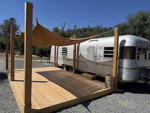 A recreational vehicle (RV) parked on a gravel surface with a wooden deck and a canopy structure.