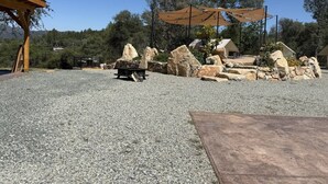 A gravel patio with a wooden pergola and a stone fire pit. - Moonshadow Flat Glamping: Gypsum Tent (Penn Valley)