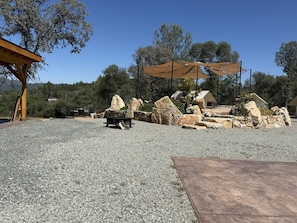 A gravel patio with a wooden pergola and a stone fire pit.