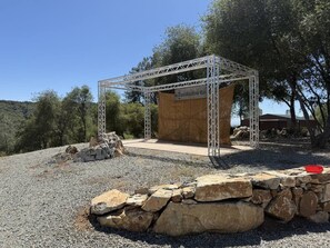 A metal structure with a wooden platform, surrounded by rocks and trees. - Moonshadow Flat Glamping: Gypsum Tent (Penn Valley)