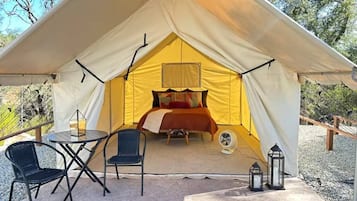 A tent with a bed, a table, two chairs, and a fan.