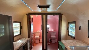 A compact bathroom with two toilets, a sink, and a shower area. - Moonshadow Flat Glamping: Gypsum Tent (Penn Valley)