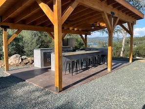 An outdoor kitchen area with a bar stool seating arrangement, a built-in grill, and a view of the surrounding landscape.